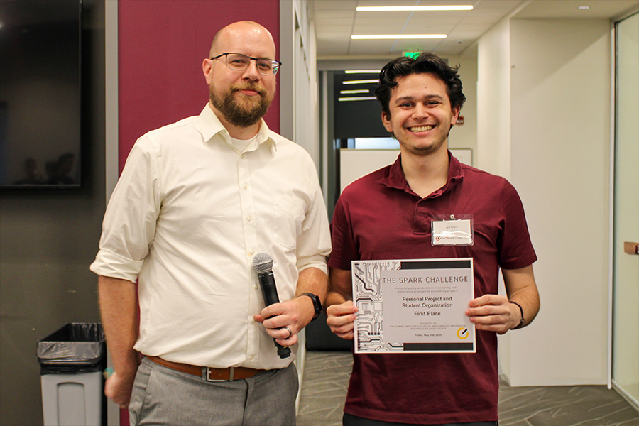 Two men proudly display a certificate in an office setting, smiling at the camera.